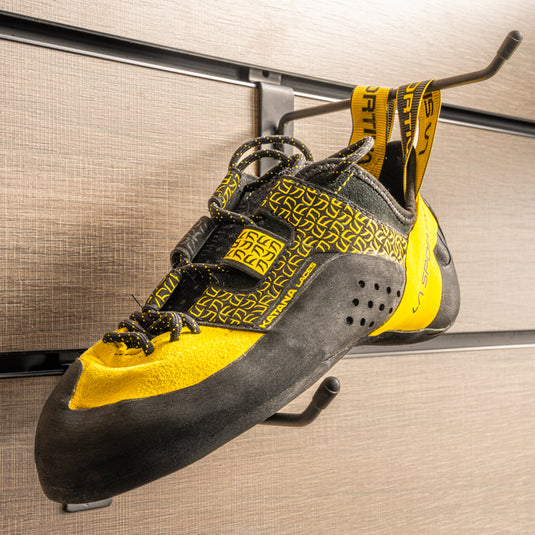 A climbing shoe, La sportiva katana Lace hanging on a black hook and with toe box balanced on another black hook against a textured metallic background.