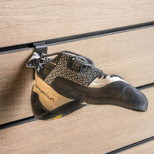 A La Sportiva katana lace women climbing shoe with a black and white heel strap loop, hanging on a wall-mounted holder against a textured background.