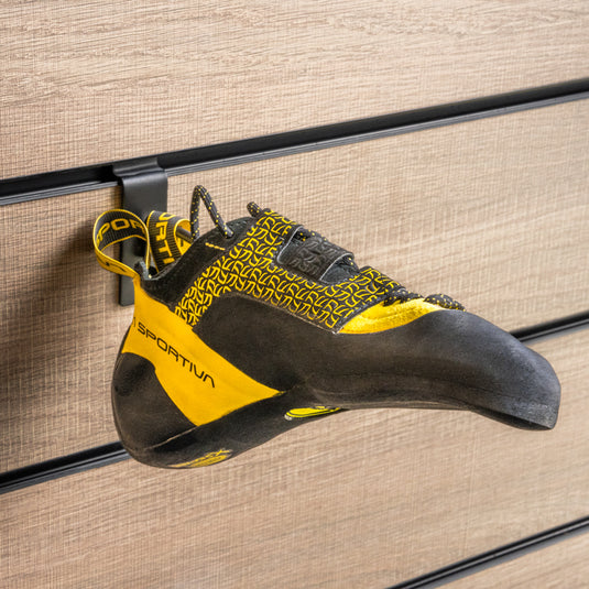 A La Sportiva Katana lace climbing shoe with a yellow and black heel strap loop, hanging on a wall-mounted holder against a textured background.