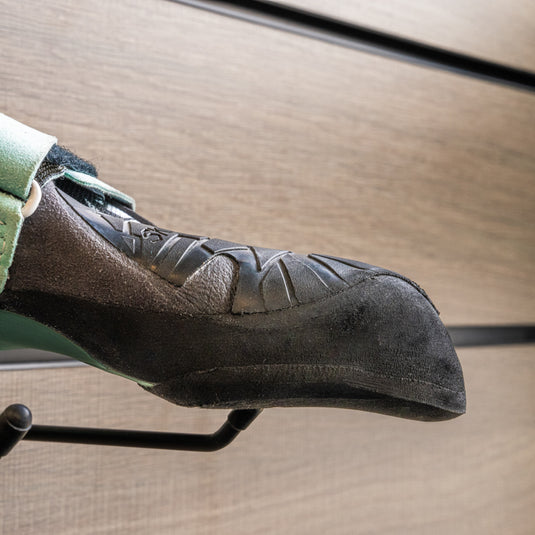 A close up La Sportiva Vegan womens toe box, resting on black wall hook against metallic background.