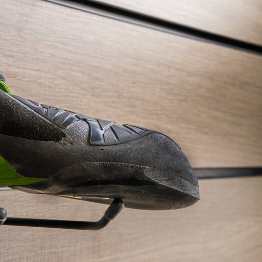A close up La Sportiva Vegan toe box, resting on black wall hook against metallic background.