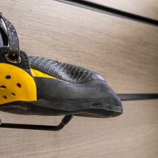 A close up La Sportiva Solution comp toe box, resting on black wall hook against metallic background.