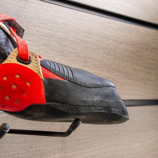 A close up La Sportiva Solution comp women toe box, resting on black wall hook against metallic background.