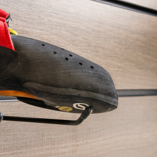 A close up Scarpa Drago toe box, resting on black wall hook against metallic background.