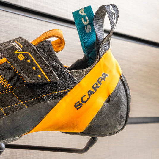A close up Scarpa instinct VS heel, resting on black wall hook against metallic background.