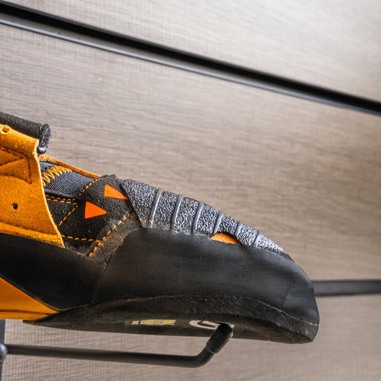 A close up Scarpa instinct VS toe box, resting on black wall hook against metallic background.