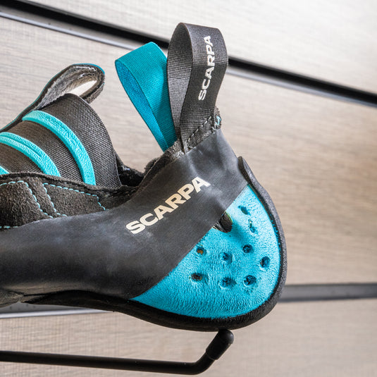 A close up of Scarpa Instinct S blue heel cup, wrapped with a line in the centre of black M50 rubber resting on black hook against metallic background.