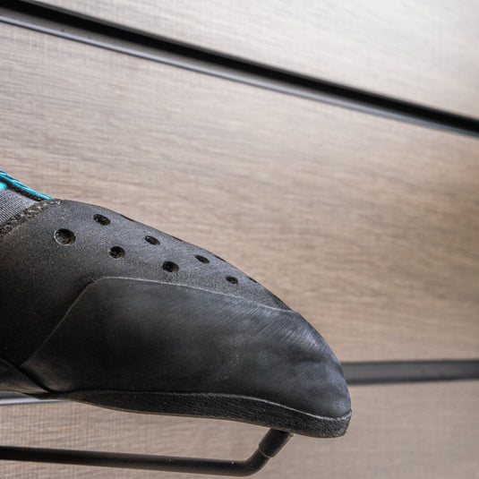 A close up Scarpa Instinct S toe box, resting on black wall hook against metallic background.