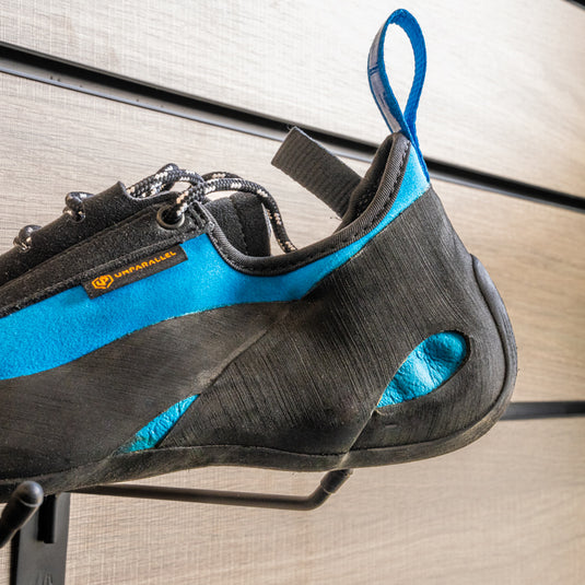 A close up Unparallel Up lace Heel, resting on black wall hook against metallic background.