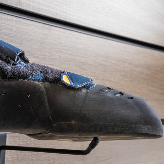 A close up La Sportiva Tarantula Boulder toe box, resting on black wall hook against metallic background.
