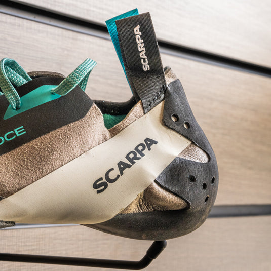 A close up Scarpa Veloce Lace WMN Heel, resting on black wall hook against metallic background.