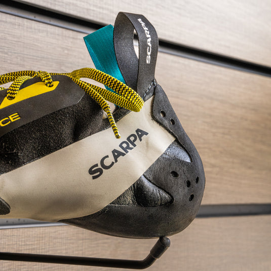 A close up Scarpa Veloce Lace Heel, resting on black wall hook against metallic background.