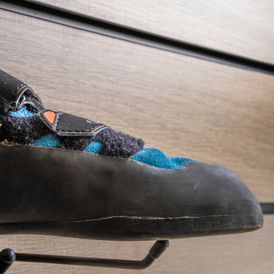 A close up La Sportiva Tarantula toe box, resting on black wall hook against metallic background.