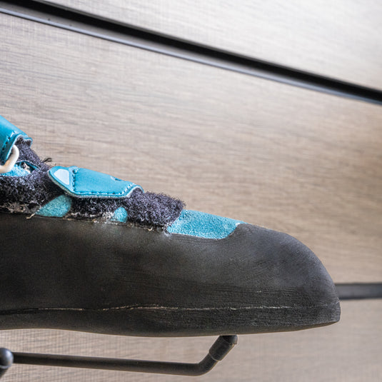 A close up La Sportiva Tarantula womens toe box, resting on black wall hook against metallic background.