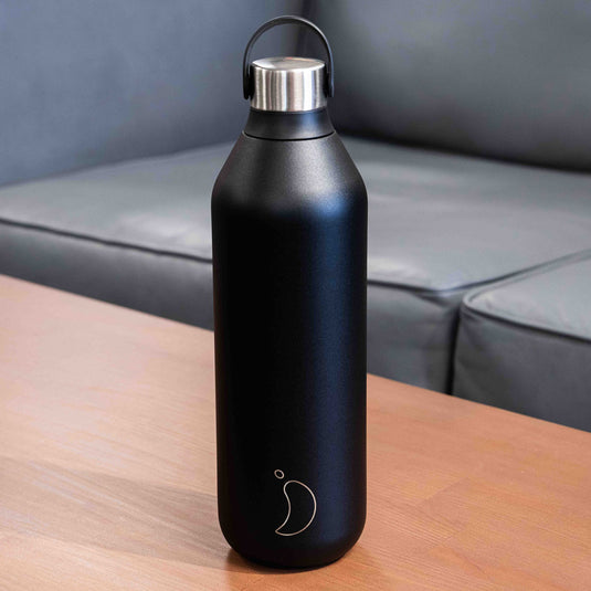 Black 1l chilly's water bottle with stainless steel lid displayed on wooden surface