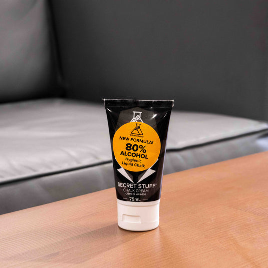 One 75ml tube of Friction Labs Secret Stuff Liquid Chalk in black and white design with a circular orange sticker with 80% alcohol text. The tube is displayed on a wooden surface.