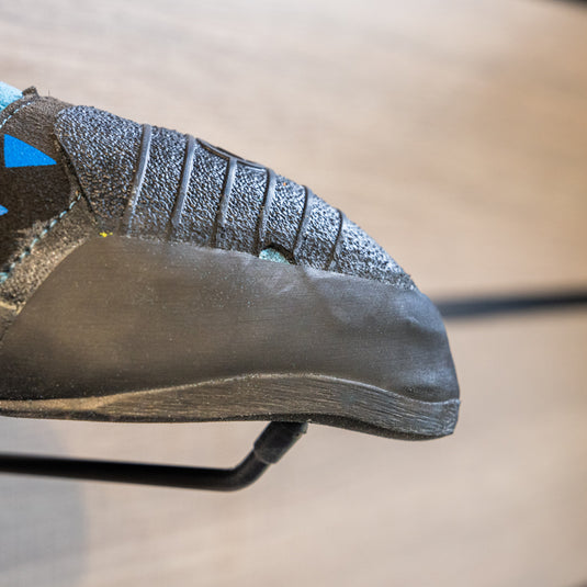 A close up Scarpa Instinct VSR toe box, resting on black wall hook against metallic background.