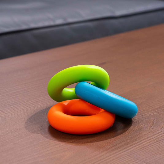 three circular forearm trainers in green, blue and orange laid on wooden surface