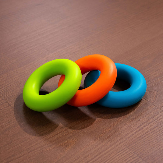 three circular forearm trainers in green, blue and orange laid on wooden surface