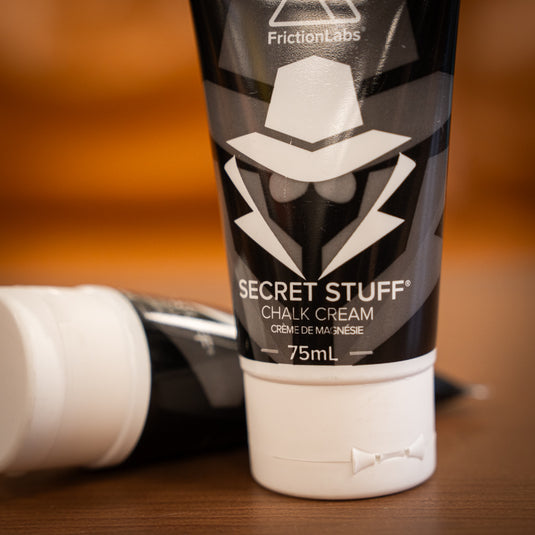 Two 75ml tubes of Friction Labs Secret Stuff Liquid Chalk in black and white design. The tube in the background is lay down, the tube in the foreground is stood up.