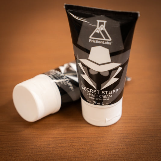 Two 75ml tubes of Friction Labs Secret Stuff Liquid Chalk in black and white design. The tube in the background is lay down and blurred, the tube in the foreground is stood up and in focus.