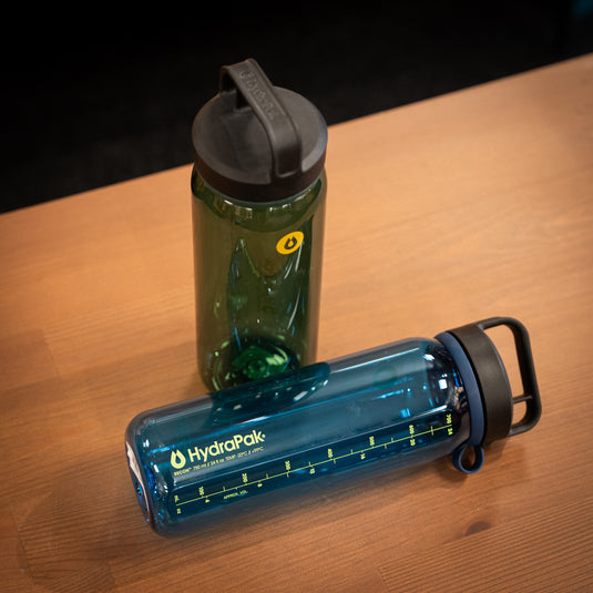 Two Recon water bottles displayed on wooden surface. One green bottle is stood up, one blue bottle is lay down.