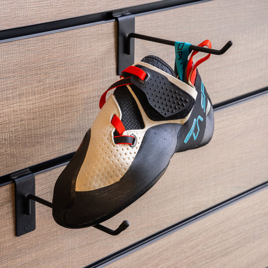 A climbing shoe, La sportiva Futura hanging on a black hook and with toe box balanced on another black hook against a textured metallic background.