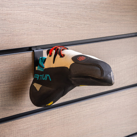 A La Sportiva Futura climbing shoe with a turquoise heel strap loop, hanging on a wall-mounted holder against a textured background.