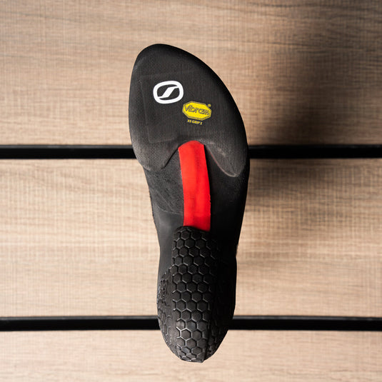 The sole of a climbing shoe, Scarpa Drago XT, showing Vibram rubber logo and split sole with red strip representing stiffer midsole.