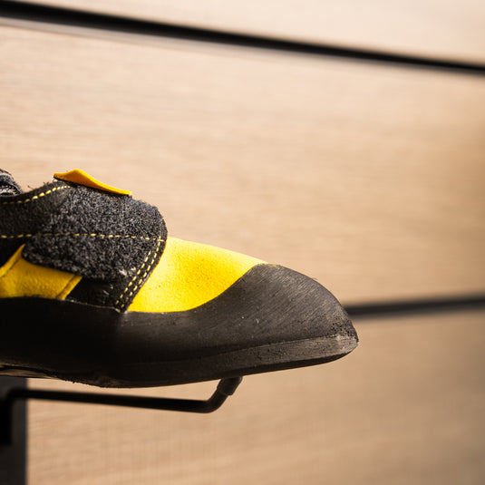 A close up La Sportiva katana Velcro toe box, resting on black wall hook against metallic background.