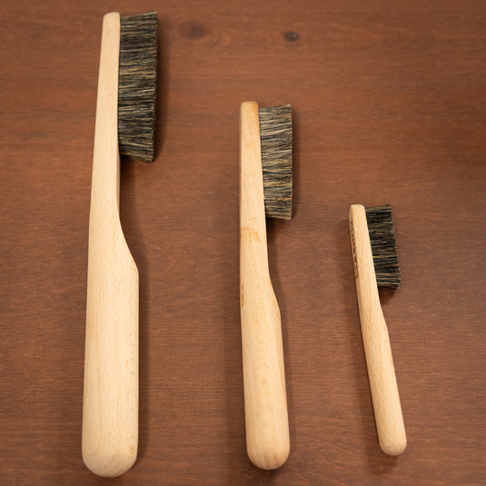 Three ClimbLab brushes of different sizes resting on wooden surface