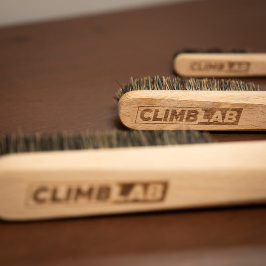 Three wooden CLIMBLAB brushes of varying size resting on a wooden surface