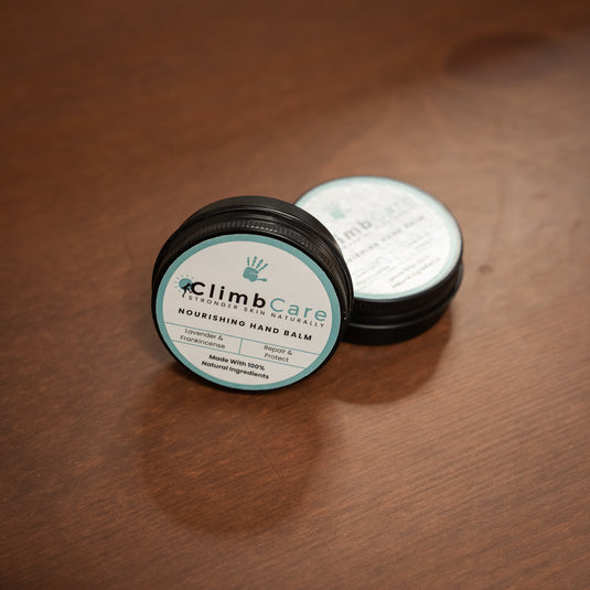 Two containers of ClimbCare nourishing hand balm laid on wooden surface in pale blue and white design.