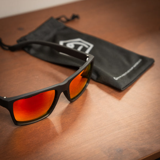 E9 Sunglasses - "Paul" laid on wooden surface with sunglasses bag with e9 logo on in black in blurredbackground