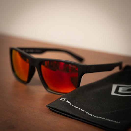 E9 Sunglasses - "Paul" laid on wooden surface with sunglasses bag with e9 logo on in black in blurredbackground