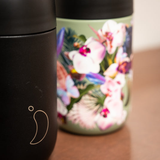 A reusable chilly's coffee cup in black beside the vibrant floral designs.