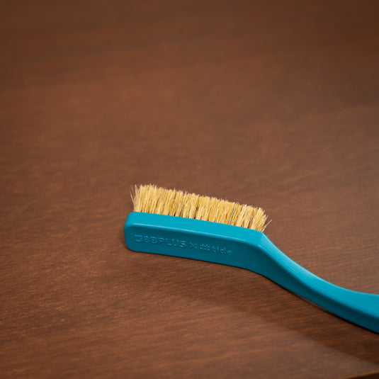8b+ save the ocean climbing brush in blue resting on a wooden surface engraved with "8Bplus X #tide" on the head of the brush