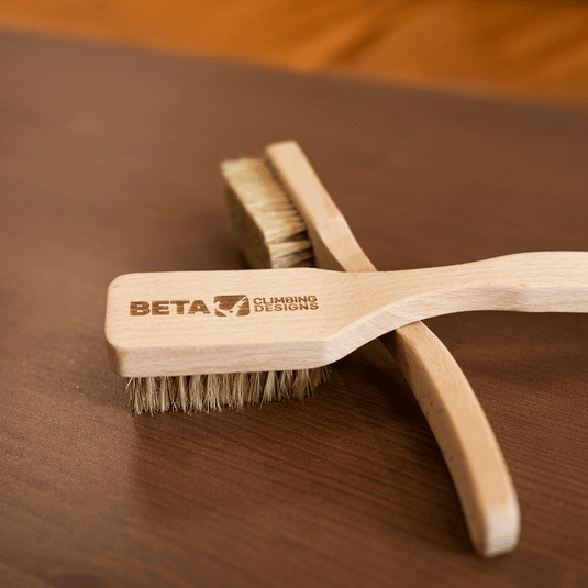 Two wooden Beta climbing brushes engraved with Beta Climbing Designs logo. Resting on wooden surface