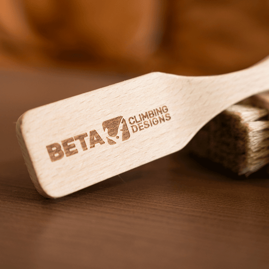 Two wooden Beta climbing brushes engraved with Beta Climbing Designs logo. Resting on wooden surface