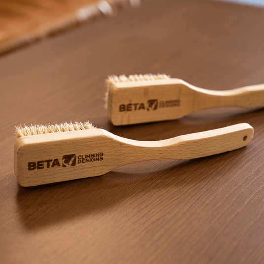 Two wooden Beta climbing brushes engraved with Beta Climbing Designs logo. Resting on wooden surface