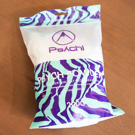 Psychi Chalk 200g in purple and green packaging with "PSYCH POWDER" text displayed lay down on wooden surface.