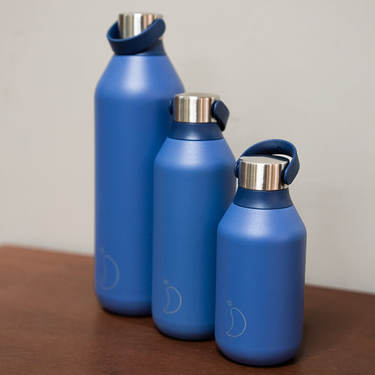 3 blue chillys bottles in different sizes displayed on wooden surface. 1L, 500ml and 350ml all with stainless steel lid.
