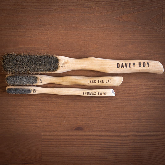 Three Silly Goat brushes showcasing the boar hair bristles and different sizes resting on wooden surface. Davey Boy, Jack the Lad, Thomas Twig are engraved on the different sized brush handles.