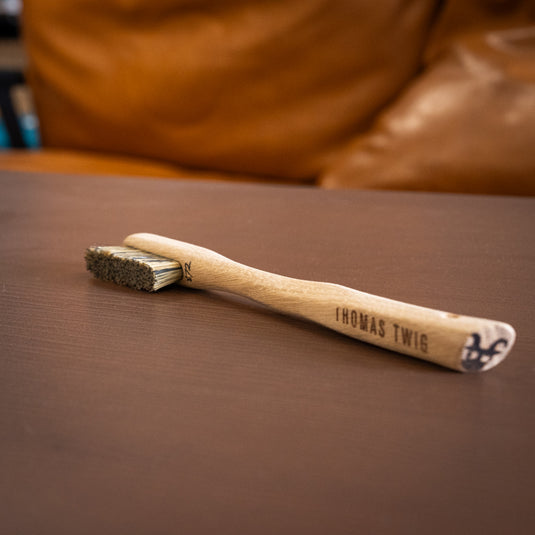 One Thomas Twig Silly Goat brush resting on wooden surface. Thomas Twig engraved on the handle and brush ID number 872