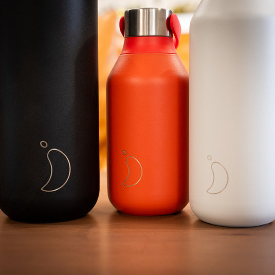 3 bottles in different sizes and colours displayed on wooden surface. Black 1L, Grey 500ml and Red 350ml all with stainless steel lid. Chilly's logo is displayed on all bottles.