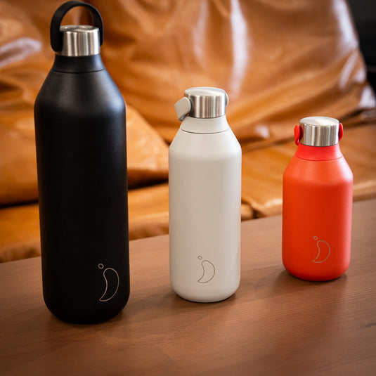 3 bottles in different sizes and colours displayed on wooden surface. Black 1L, Grey 500ml and Red 350ml all with stainless steel lid.