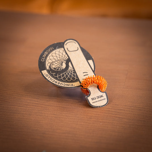 Bright Orange finger massager displayed on a cardstock with a finger design and climbskin logo, resting on wooden table.