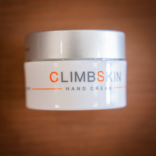 A white container of ClimbSkin hand cream with a silver lid, on a wooden surface.