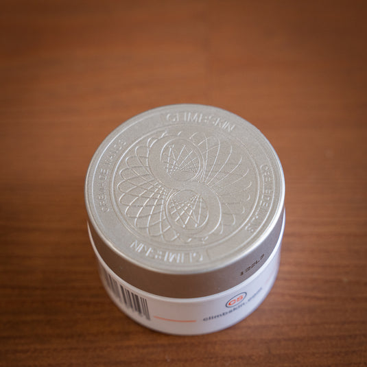 A white container of ClimbSkin hand cream with a silver lid, on a wooden surface.