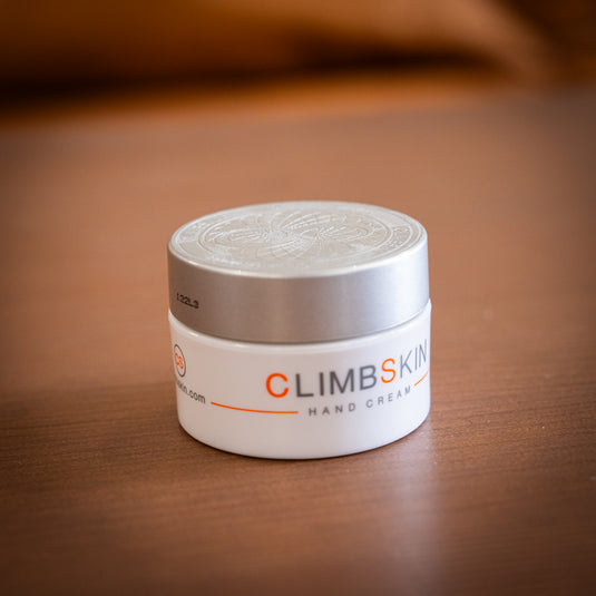 A white container of ClimbSkin hand cream with a silver lid, on a wooden surface.